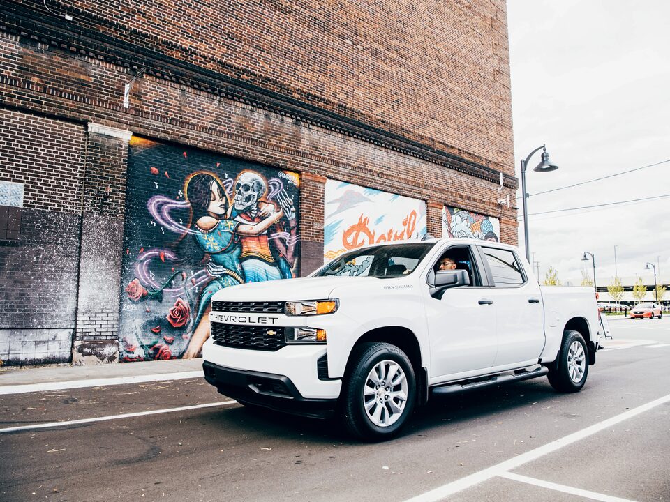 Freddy Diaz in a white Silverado on a Detroit street next to one of Freddy’s colorful murals.