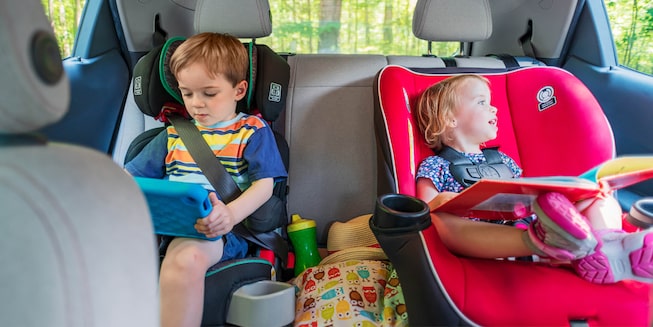 Two children sit in car seats in the backseat of a Bolt EV. One is using a tablet and the other is holding a book and looking out the window.