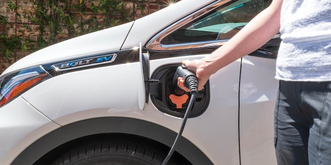 A woman’s arm is seen plugging a charging cable into the side of a white Bolt EV.