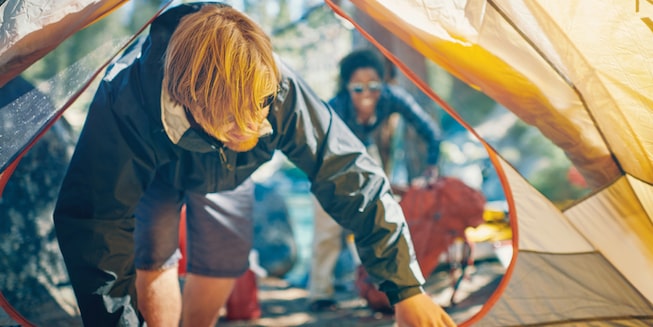 A man climbing into a tent while setting up camp.