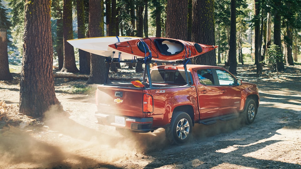 Una Chevy Colorado con dos kayaks en el portaequipajes conduce por el bosque.