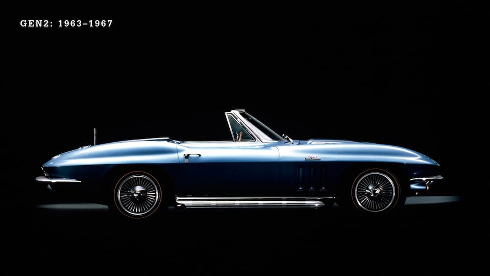 Un Corvette convertible de 2.ª generación (C2, 1963-1967) en Azul con la capota baja visto desde un costado contra un fondo negro.