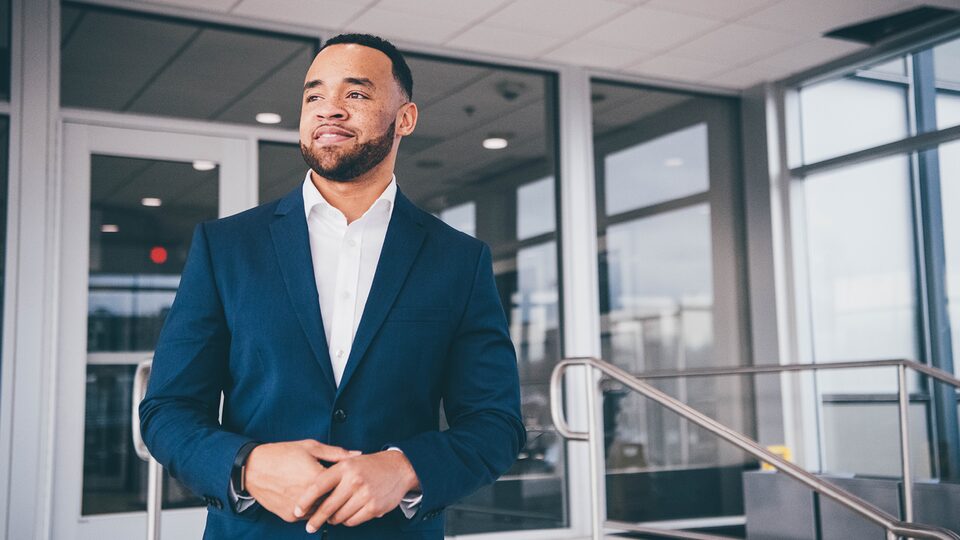 Charles Muse, wearing a button-down shirt and sport coat, stands at an entrance to the General Motors Tech Center in Warren, Michigan.
