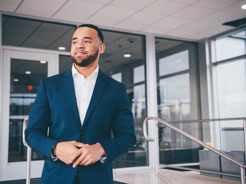 Charles Muse, wearing a button-down shirt and sport coat, stands at an entrance to the General Motors Tech Center in Warren, Michigan.