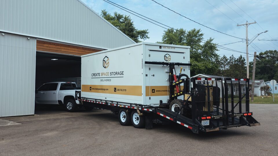 A white Silverado 3500 HD hauling a large trailer pulls into a warehouse building through a garage opening.