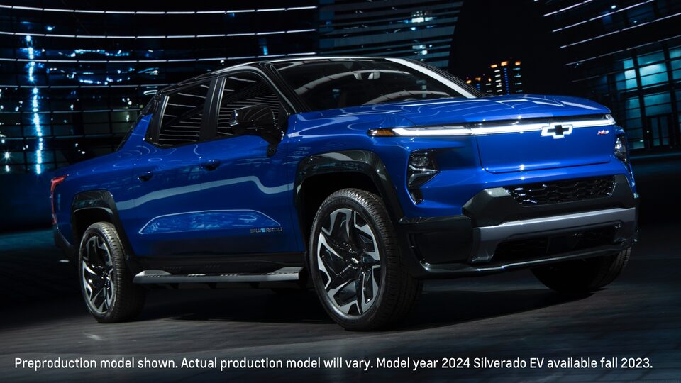 A blue Silverado EV at night on an urban street with the lights from tall buildings shining in the background.