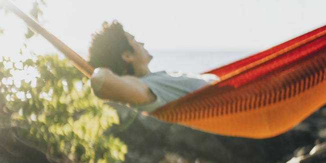 A man relaxes in a red and orange hammock.