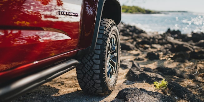 A close-up of a tire on the Chevrolet Colorado ZR2 on rocky terrain, with the ocean in the background.