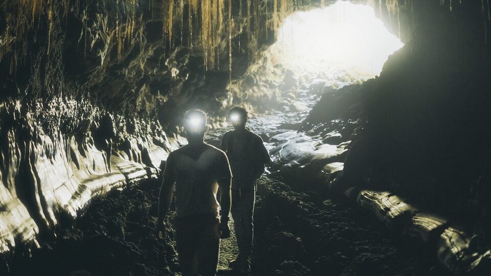 Two men wearing headlamps explore the inside of Kaumana Caves.