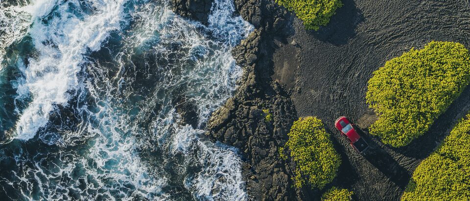 An aerial shot of a red Chevrolet Colorado ZR2 parked near the edge of a rocky landscape with water rushing past.