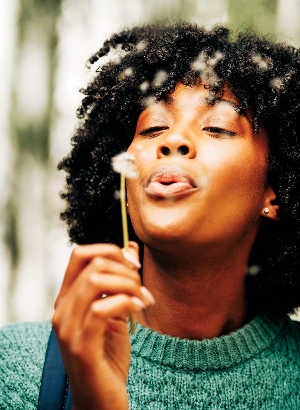 A person blows the seeds from a dandelion puff.