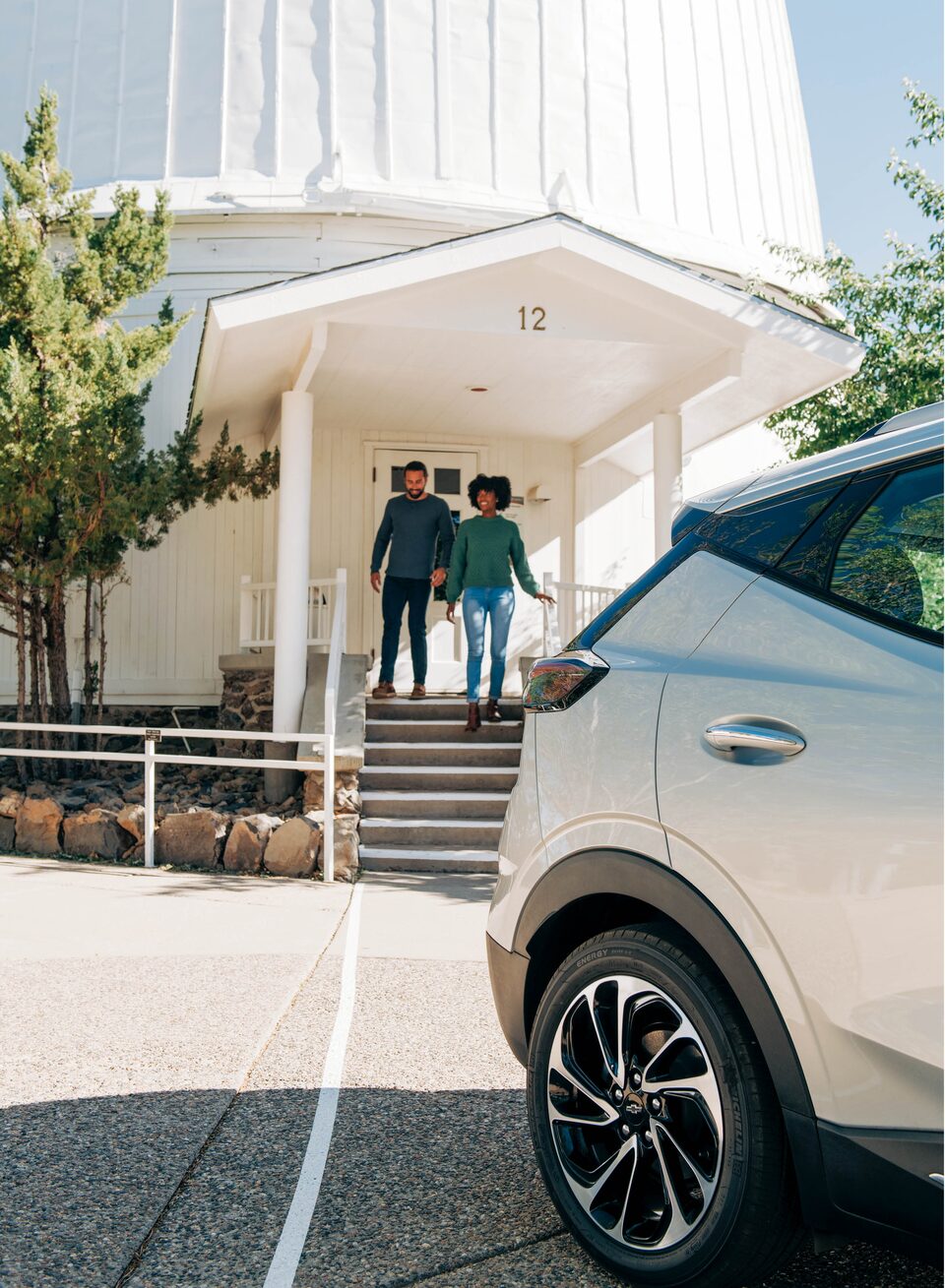 Two people come out of an astronomy observatory and walk down steps toward a Bolt EUV in the parking lot.