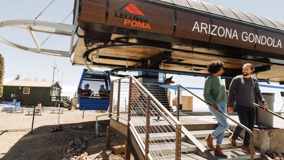 Two people descend the steps after taking a sightseeing ride on a ski lift gondola in the summer.