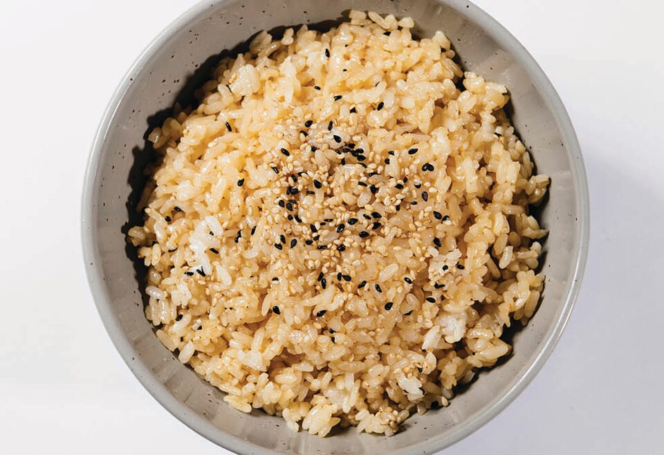Tazón de color blanco visto desde arriba lleno de arroz con una tonalidad amarilla-beis y rociado con pequeñas semillas de color negro y marrón.