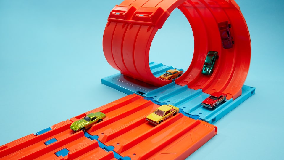 Several Hot Wheels on a fivelane orange Hot Wheels track with a loop.