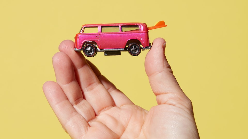 A hand holding a pink Hot Wheels bus