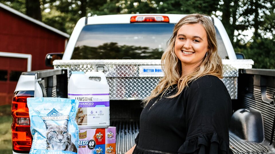 Scout Bagley stands at the open tailgate of her Silverado, which has several bags of pet food in the bed.