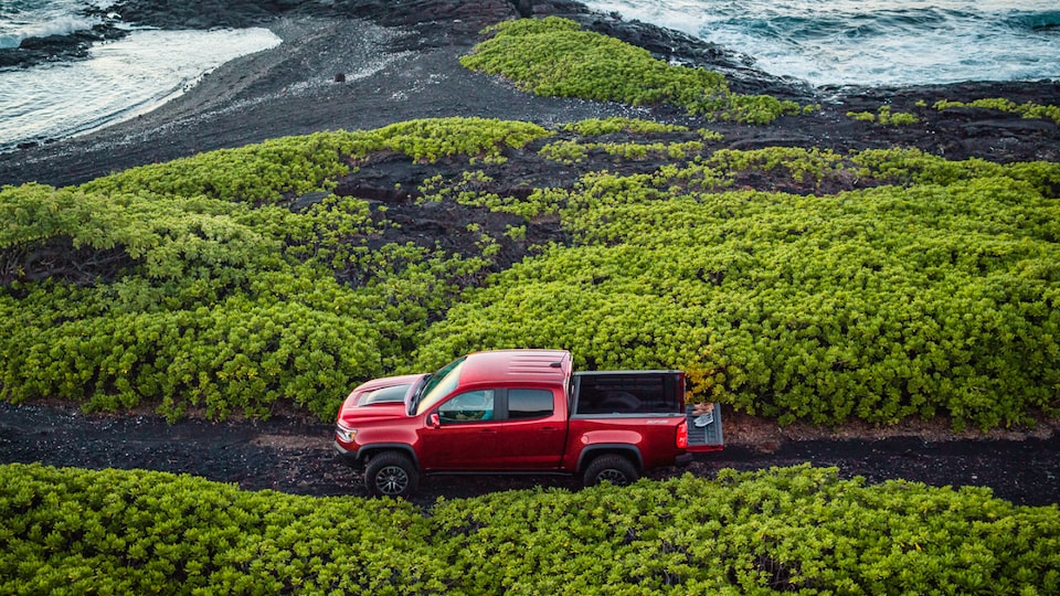A side view of a red Chevrolet Colorado ZR2 stopped on a narrow road with greenery on either side.