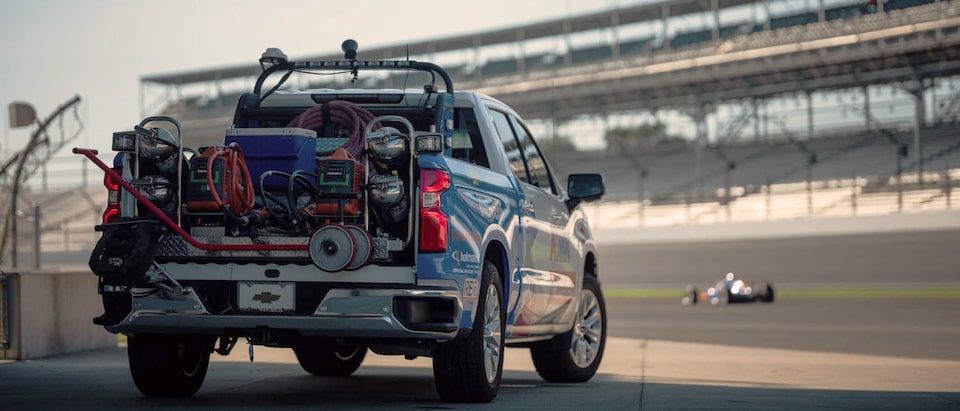 Rear view of a Chevrolet Silverado outfitted with equipment in the bed of the truck, with the race track is in the background.