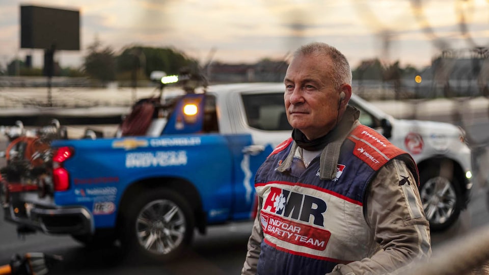 Tim Baughman wears a safety suit that reads “AMR IndyCar Safety Team.” There is a Chevrolet Silverado in the background.