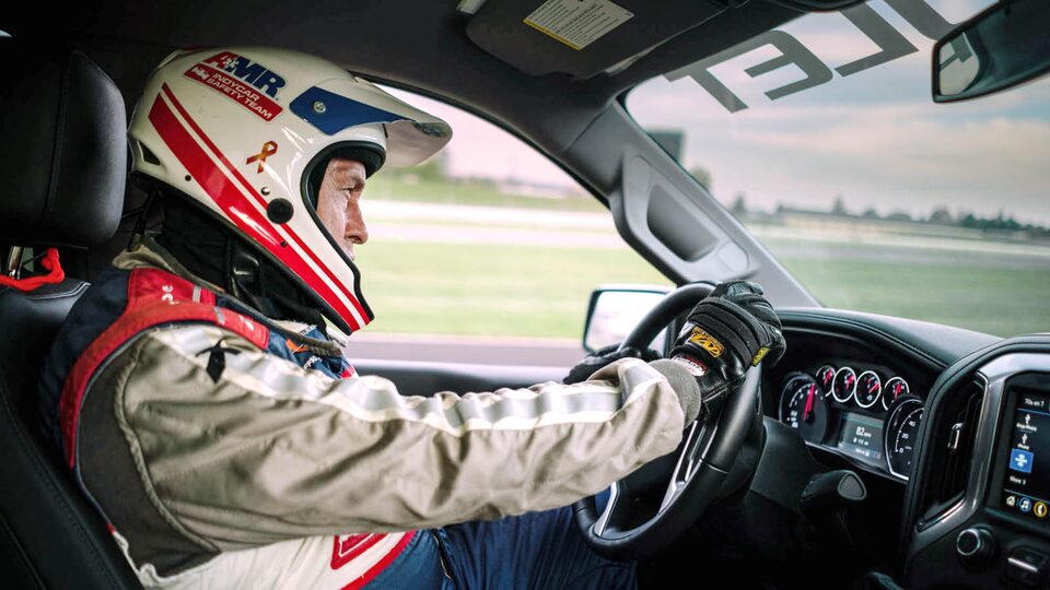 Tim Baughman wears a helmet and sits in the driver’s seat of the Chevrolet Silverado.