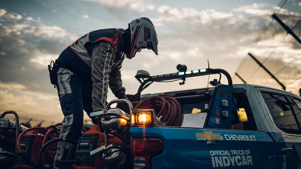Tim Baughman wears a safety suit and helmet and handles equipment while standing in the bed of a Chevrolet Silverdo.