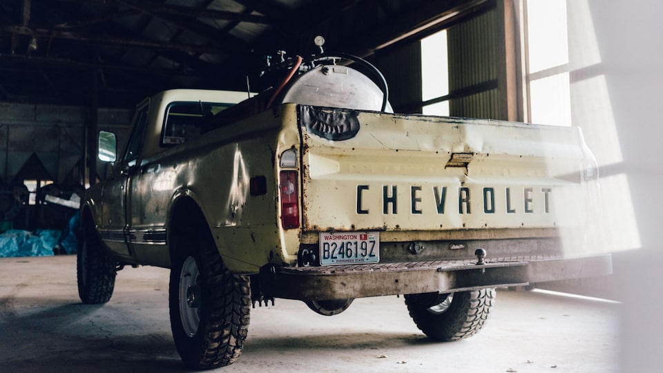 A view of the tailgate of an old tan Chevy truck with equipment in the bed.