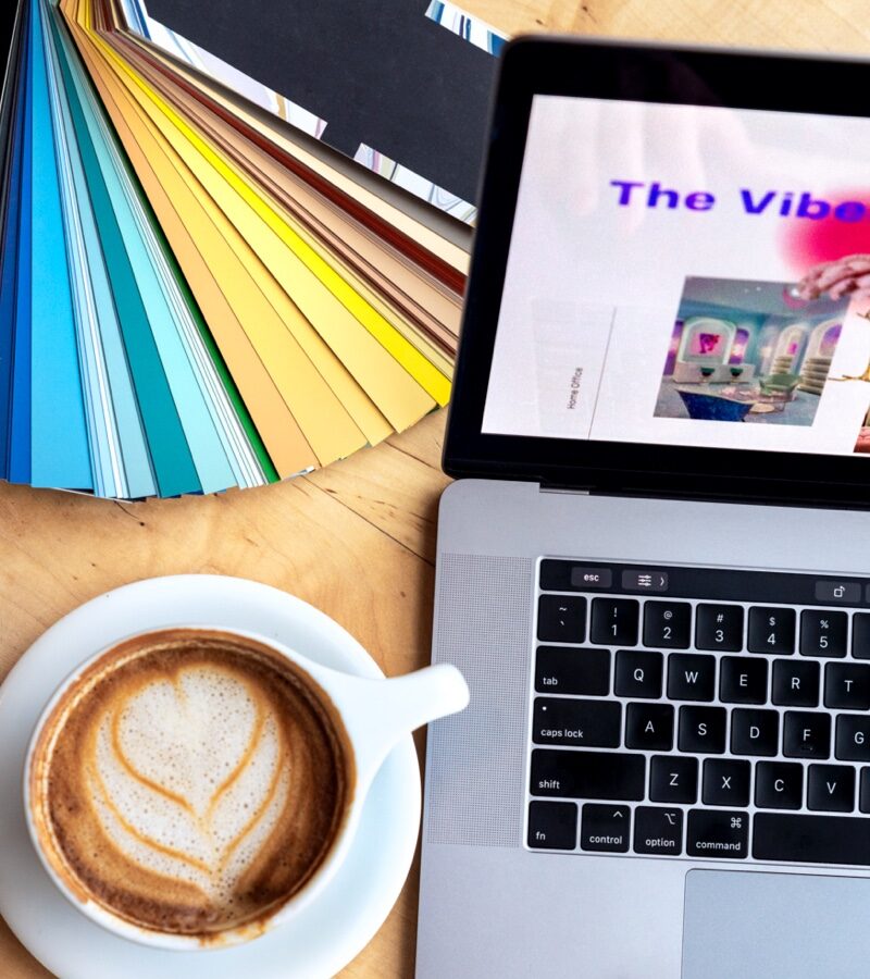 A cup of coffee, a laptop, and an array of color swatches sit on a desk.