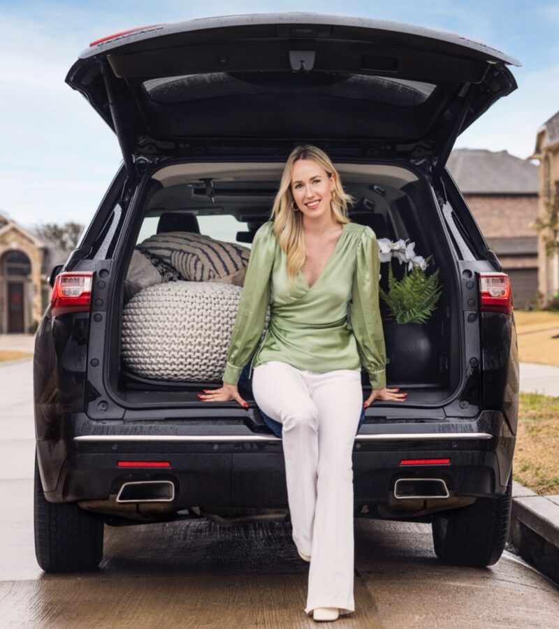 Jodi Gaines sits in the open back hatch of her black Chevy Traverse with some home decorating objects inside.