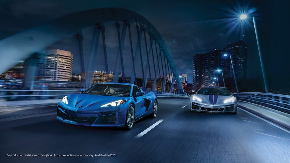 Un Corvette E-Ray azul cruza un puente por la noche al lado de un Corvette E-Ray gris con franjas de carrera azules.