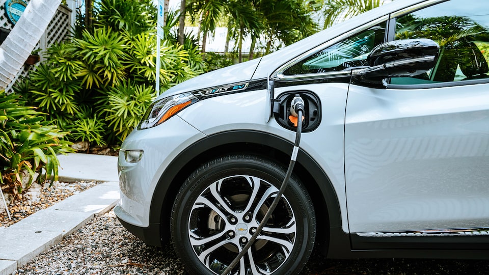 Un Bolt EV en Plata Hielo Metálico enchufado a un cargador en un estacionamiento.