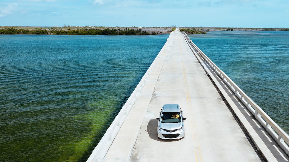 Visto desde arriba, a un Bolt EV en Plata Hielo Metálico que va por una calzada en los Cayos de Florida.