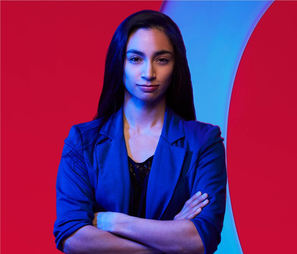 A head and shoulders shot of Kristine Bartz who looks at the camera as she stands in front of a red and blue background.