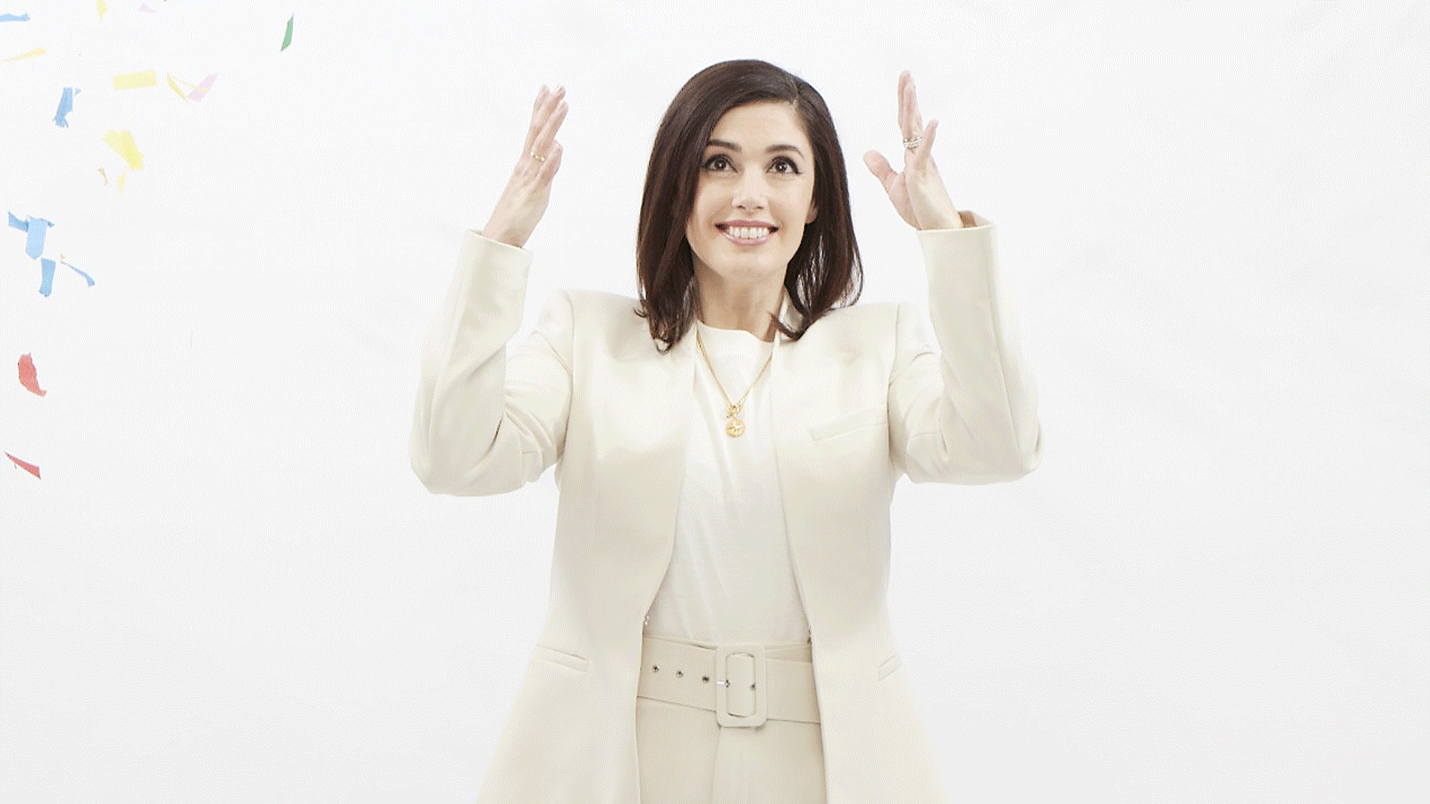 An animation showing Jennifer Widrick dressed in white and standing in front of a white background while she throws handfuls of colorful confetti into the air.