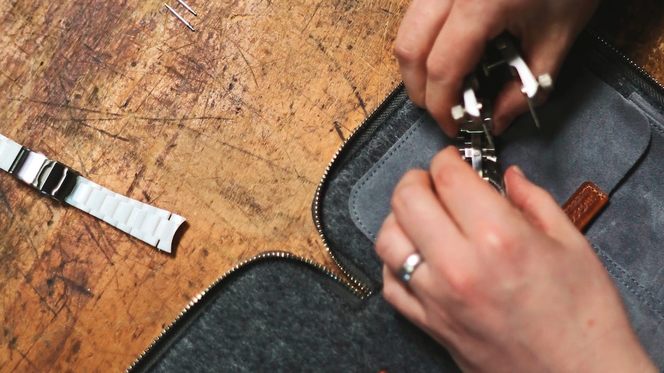 Primer plano de manos trabajando con una herramienta sobre una funda para relojes casi terminada.
