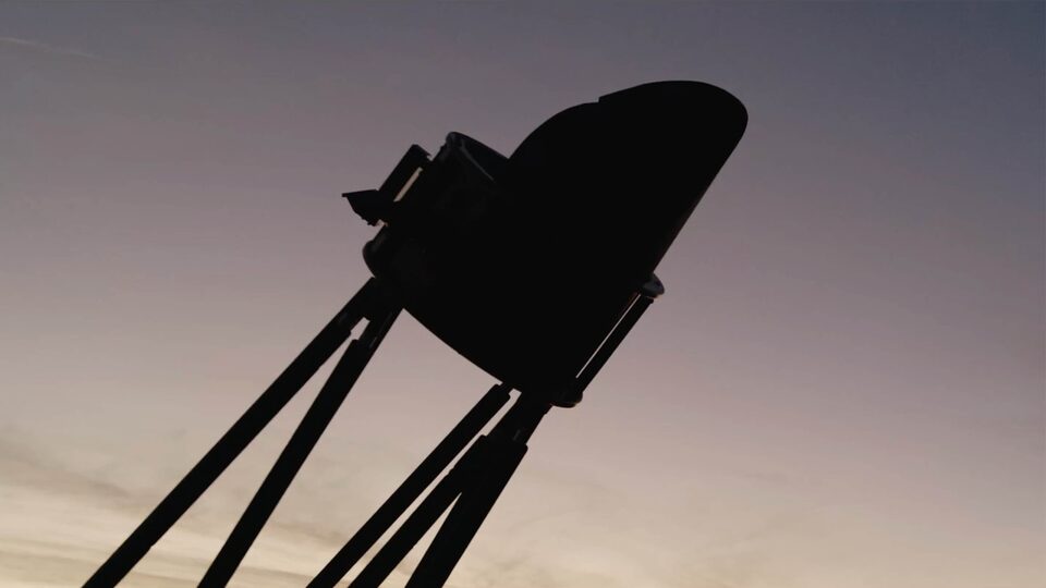 A part of a large telescope is silhouetted against the sky at dusk.