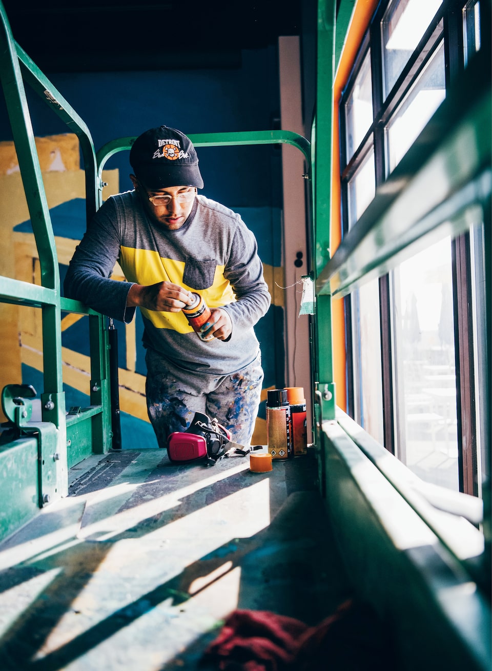 Freddy Diaz leans on some scaffolding inside a Detroit building as he fiddles with a spray can of paint.