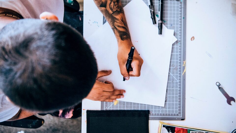 Seen from above, Freddy draws on a sheet of paper on a drafting board.
