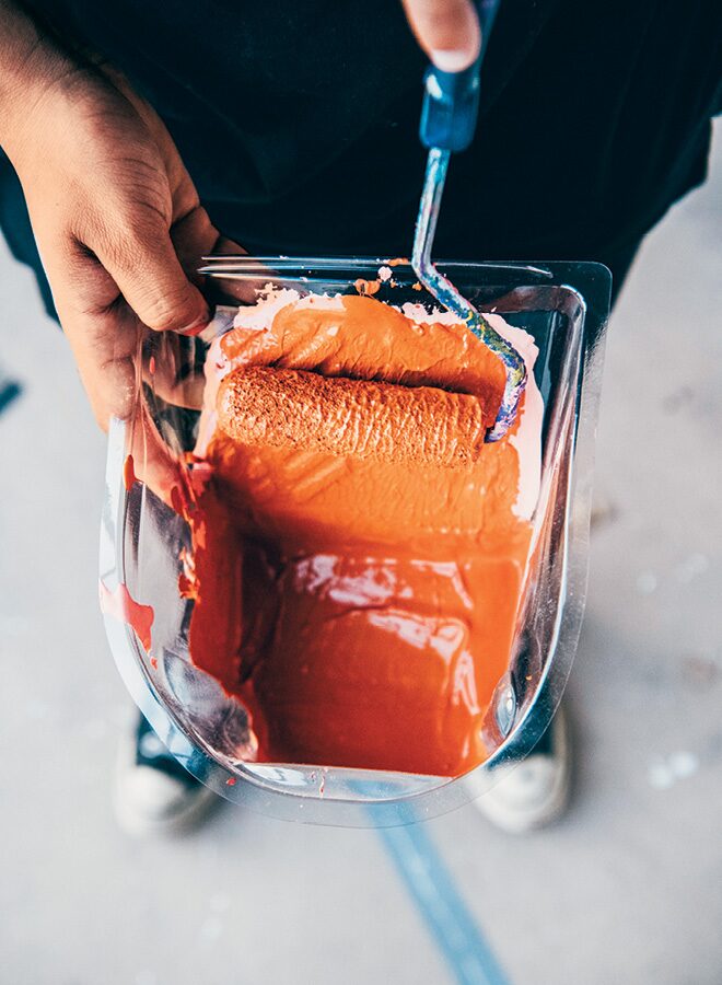 Seen from above, Freddy draws a small paint roller through a container of orange paint.