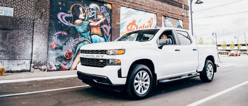 Freddy Diaz in a white Silverado on a Detroit street next to one of Freddy’s colorful murals.