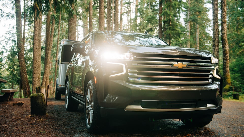 A black 2021 Chevy Tahoe pulls an Airstream Basecamp X trailer through a wooded area.