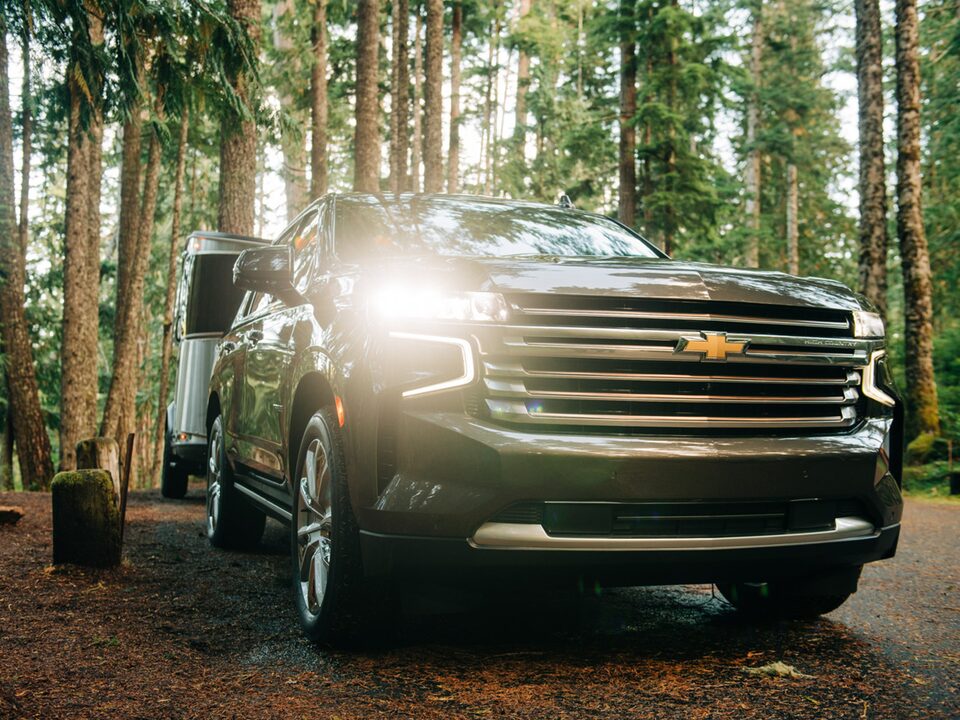 A black 2021 Chevy Tahoe pulls an Airstream Basecamp X trailer through a wooded area.
