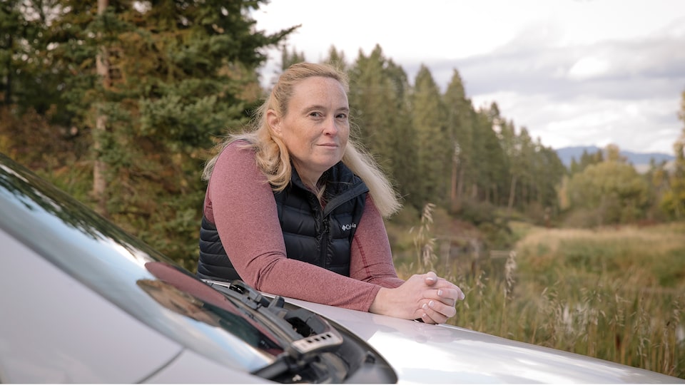 OnStar Member Jennifer Allen stands outside her truck leaning on the hood in a scenic area with evergreen trees in the background.