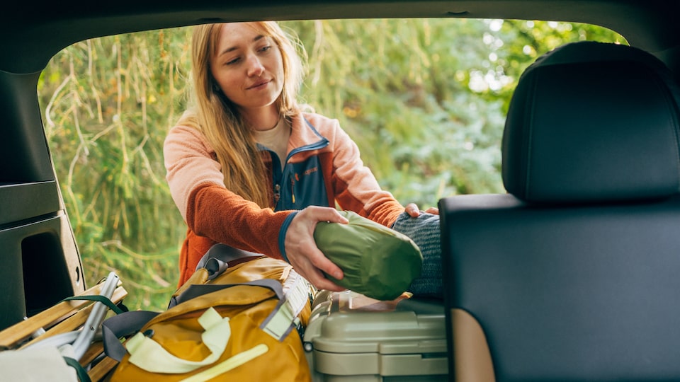 From inside the vehicle, a person is seen standing at the open hatch of a Trailblazer loading camping gear into the back.