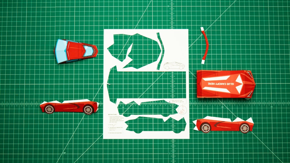 La plantilla de papel para el modelo Corvette 2020 está sobre el tablero verde de un artista con las piezas individuales cortadas y apoyadas sobre el tablero. El video que acompaña muestra el armado.