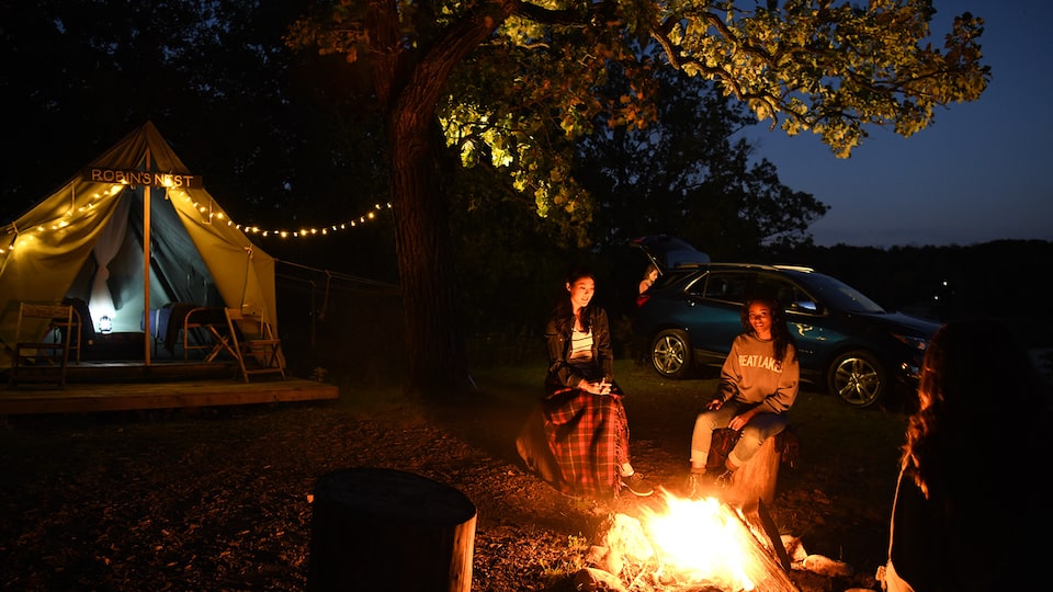 Three friends sit around a bonfire at night with a Chevrolet Equinox in the background.