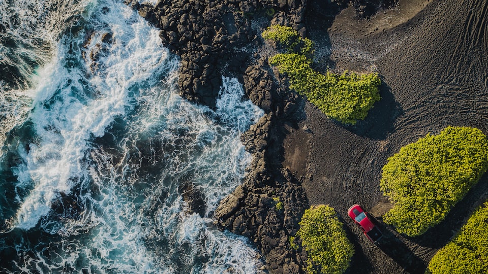 An aerial shot of a red Chevrolet Colorado ZR2 parked near the edge of a rocky landscape with water rushing past.