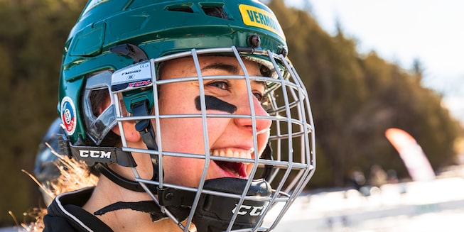 A close-up of a woman in a hockey helmet and face protection.