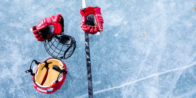 A pair of hockey gloves, a helmet, face protection, and a stick sit on the ice.