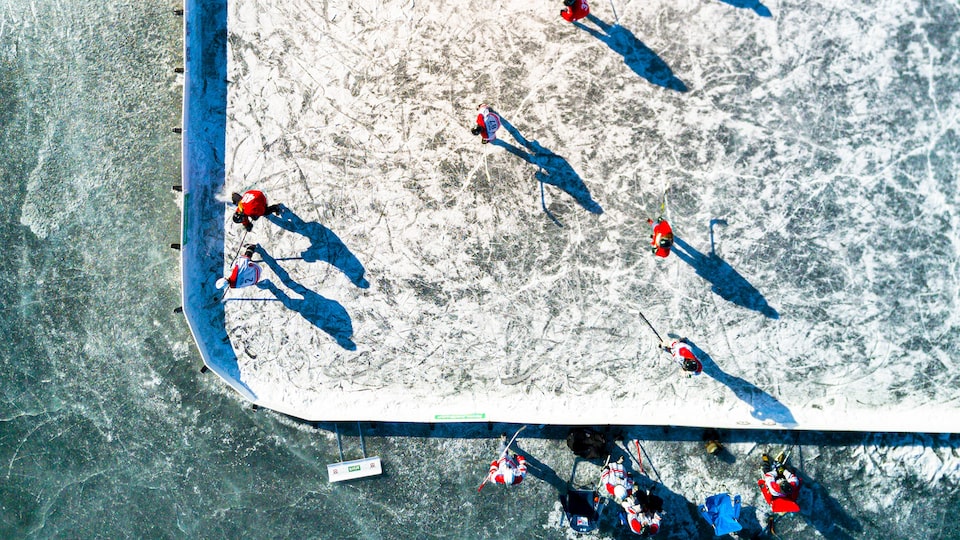 An aerial view of a group of people playing hockey on an enclosed outdoor rink.
